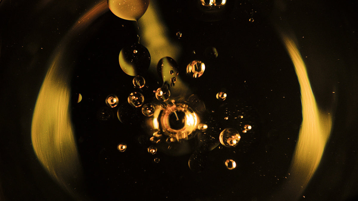 Macro of amber oil droplets suspended in liquid against a dark background with a golden glow.