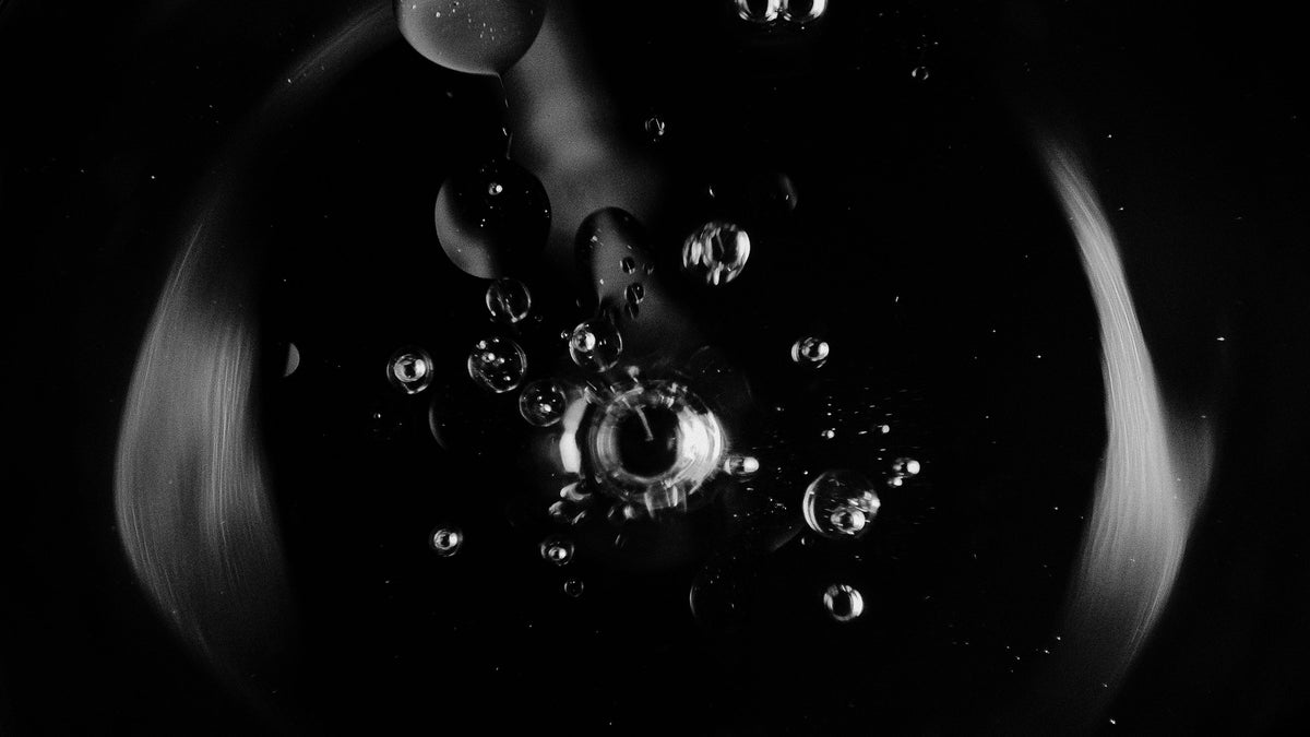 Black-and-white macro of oil droplets suspended in liquid against a dark backdrop.