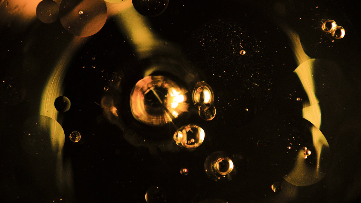 Macro of amber oil droplets clustered around a bright glow in dark liquid.