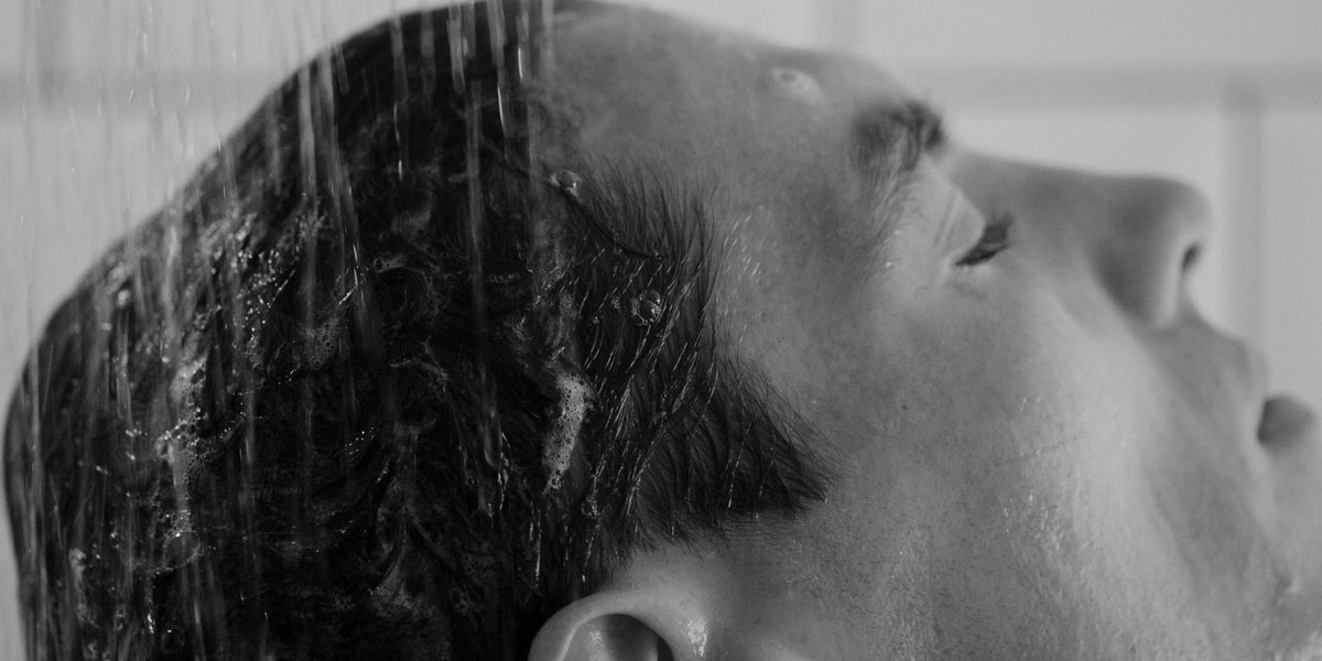 Black and white side profile of a man under the shower with water streaming through his hair.