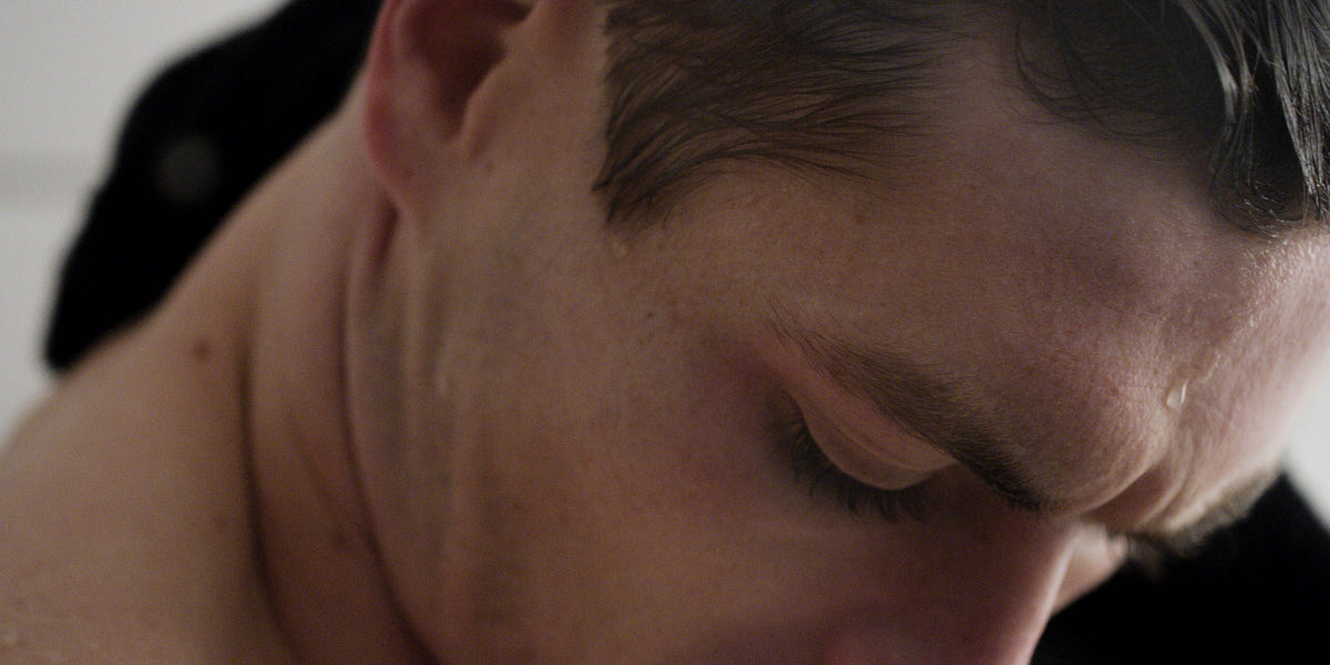Close-up of a man's forehead and damp hair as he looks down, a dark towel draped over one shoulder.