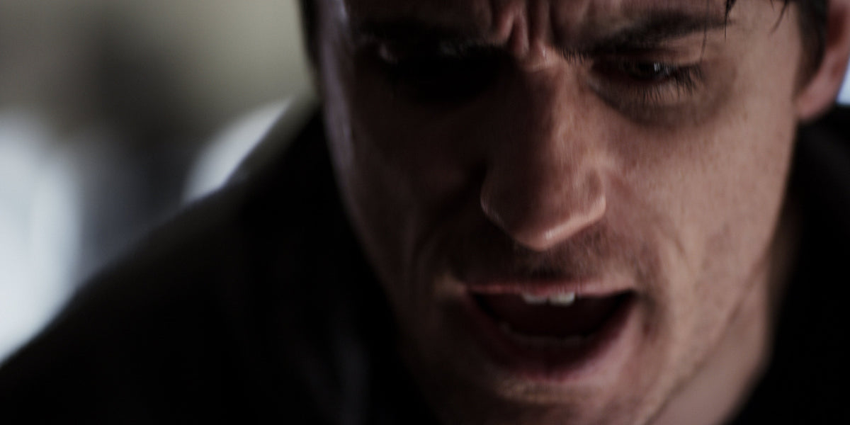 Extreme close-up of a man's nose, mouth and brow looking down in dim, moody light.