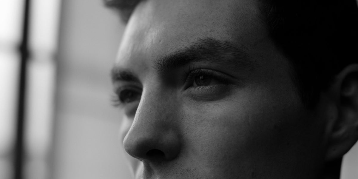 Black and white three-quarter close-up of a young man's eye, brow and cheek in soft window light.