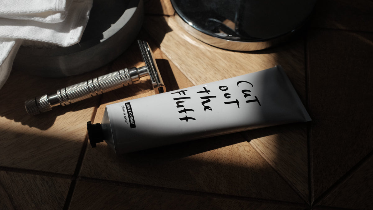 Shave cream tube and safety razor on warm wooden parquet, lit by a shaft of sunlight.