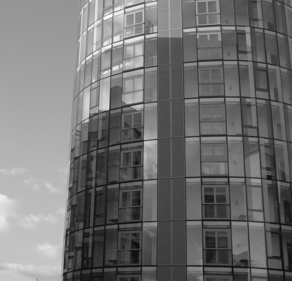 Black and white shot of a curved glass-clad tower with reflective windows wrapping around its facade.