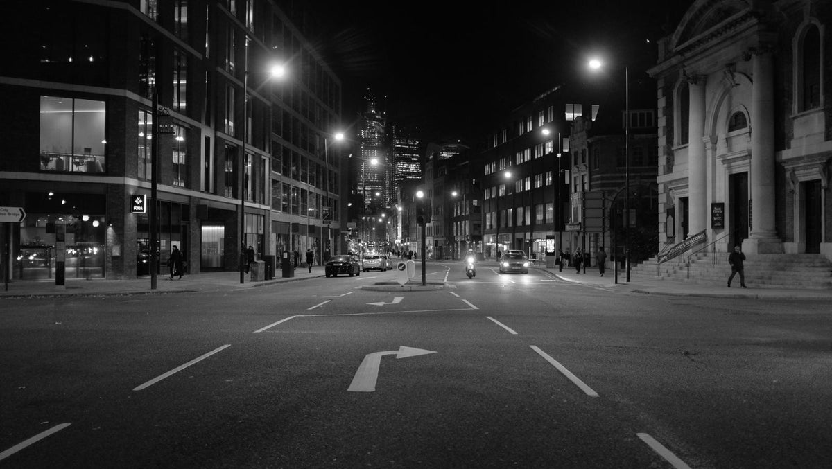 Black and white empty London street at night with classical and modern buildings, the Shard rising in the distance.